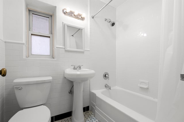 bathroom with toilet, a wainscoted wall, a sink, tile walls, and shower / bath combination with curtain