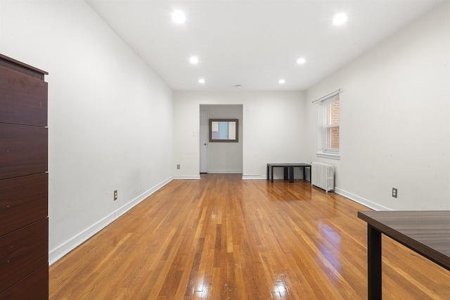 empty room with light wood-type flooring, baseboards, radiator heating unit, and recessed lighting