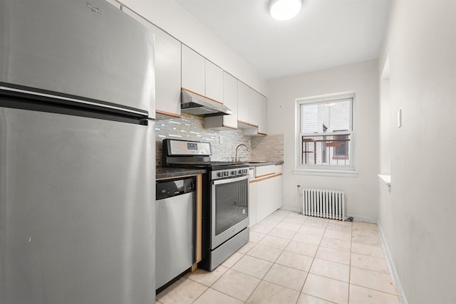 kitchen with radiator, stainless steel appliances, under cabinet range hood, white cabinetry, and tasteful backsplash