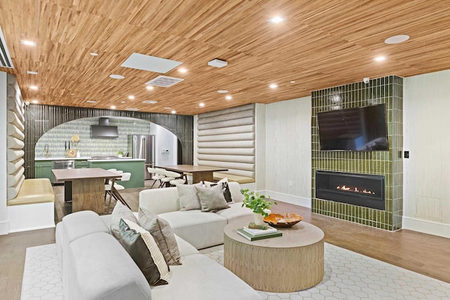 living room with log walls, light wood-type flooring, a tile fireplace, and wooden ceiling