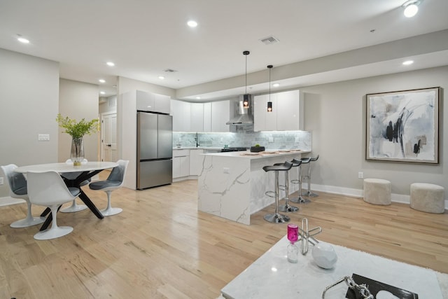 kitchen with white cabinetry, wall chimney exhaust hood, light hardwood / wood-style flooring, stainless steel fridge, and pendant lighting