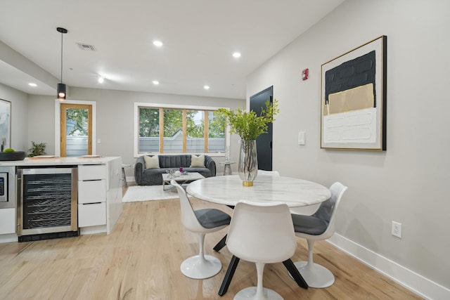 dining room with bar, wine cooler, and light hardwood / wood-style flooring