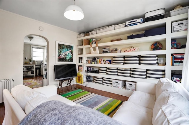 living area featuring arched walkways, wood finished floors, radiator heating unit, and ornamental molding