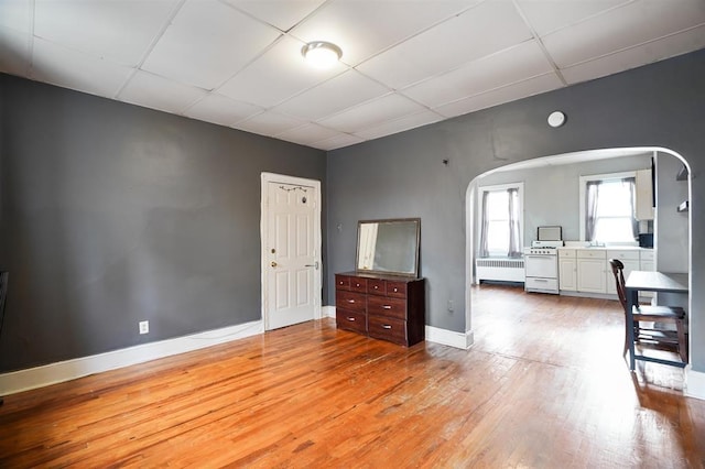 interior space featuring arched walkways, light wood-style floors, a drop ceiling, and radiator