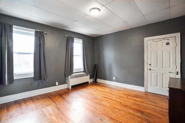 spare room with a drop ceiling, radiator, and light wood-style floors