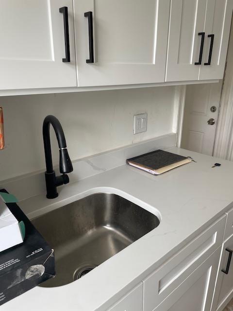 kitchen view of a sink, white cabinetry, and light stone counters