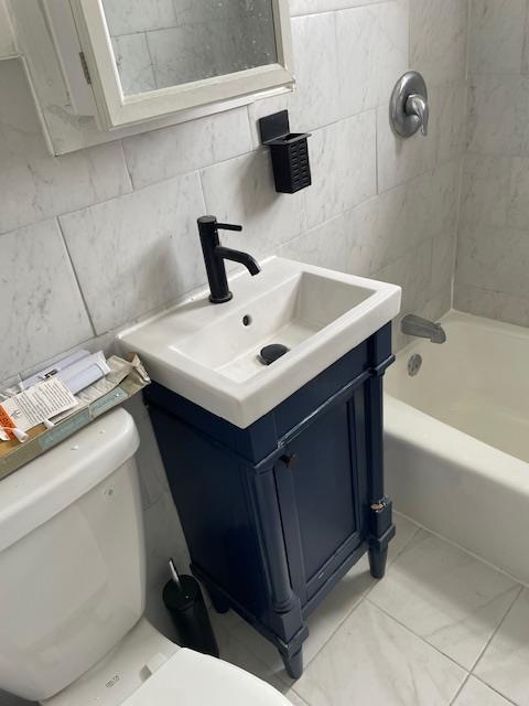 bathroom featuring toilet, vanity, tile walls, shower / tub combination, and tile patterned flooring