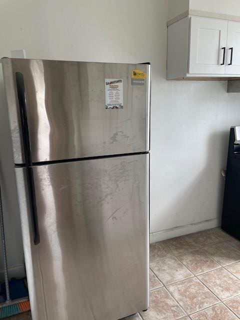 kitchen with freestanding refrigerator, white cabinetry, range, and light tile patterned floors