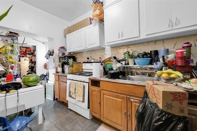 kitchen featuring white cabinets, a sink, light countertops, decorative backsplash, and white range with gas cooktop