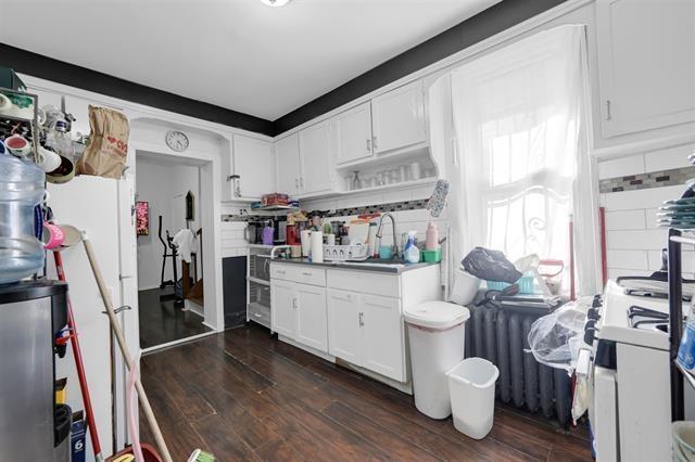 kitchen with white cabinets, a sink, radiator, decorative backsplash, and dark wood-type flooring