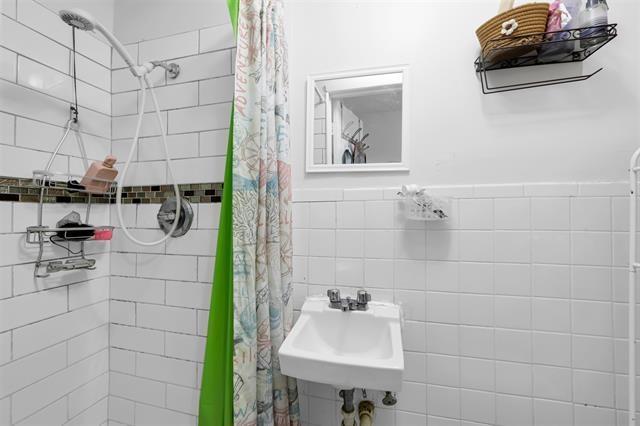 full bath featuring tile walls, a sink, wainscoting, and tiled shower