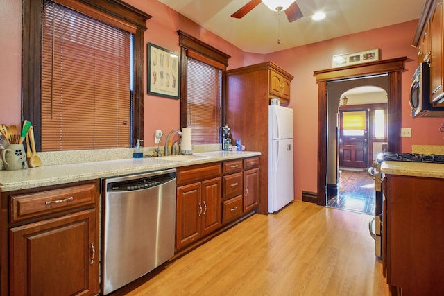 kitchen featuring sink, light hardwood / wood-style floors, ceiling fan, stainless steel appliances, and light stone countertops