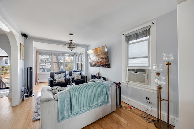 living room with arched walkways, light wood-style flooring, cooling unit, and baseboards