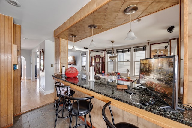 kitchen with dark tile patterned floors, decorative light fixtures, dark stone counters, a kitchen bar, and arched walkways