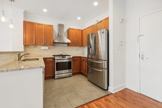 kitchen with appliances with stainless steel finishes, a sink, light stone countertops, wall chimney range hood, and backsplash