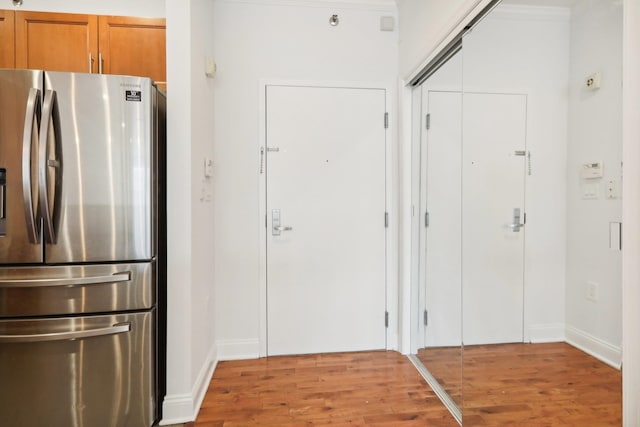 kitchen featuring light wood-style flooring, brown cabinetry, freestanding refrigerator, and baseboards