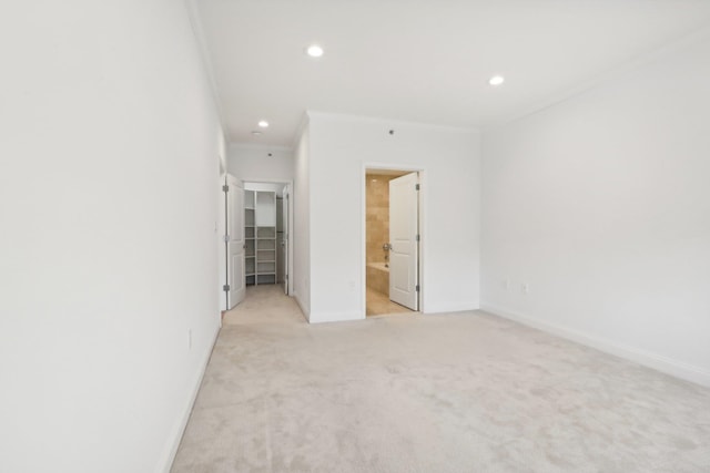 unfurnished bedroom with a walk in closet, crown molding, recessed lighting, light colored carpet, and baseboards