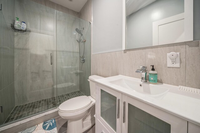 bathroom with toilet, vanity, tile walls, and a shower with door