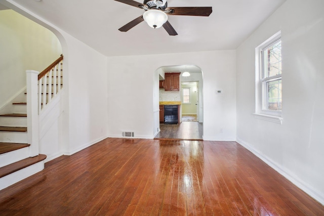 unfurnished living room featuring a wealth of natural light, arched walkways, and dark wood-style flooring