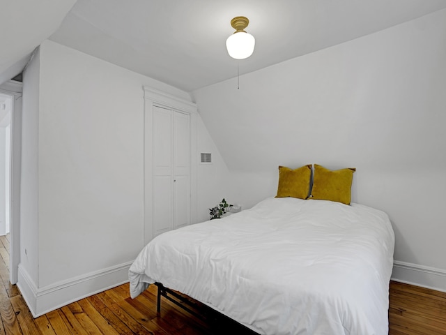 bedroom with lofted ceiling, visible vents, baseboards, and wood finished floors