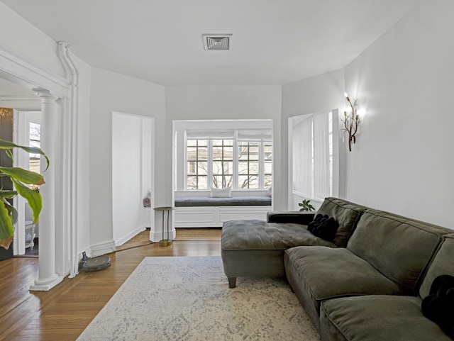 living room featuring decorative columns, visible vents, and wood finished floors