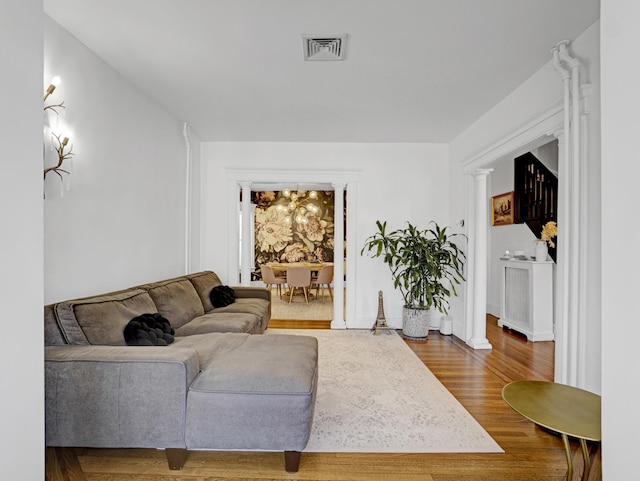 living room featuring wood finished floors, visible vents, and ornate columns