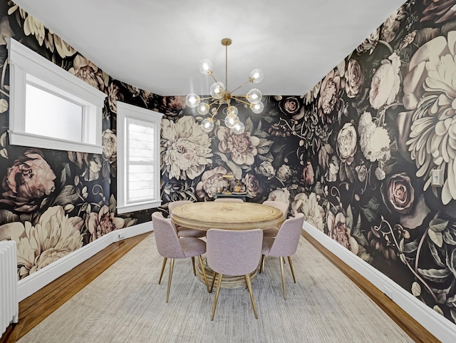 dining space with a notable chandelier, wood finished floors, baseboards, radiator, and wallpapered walls