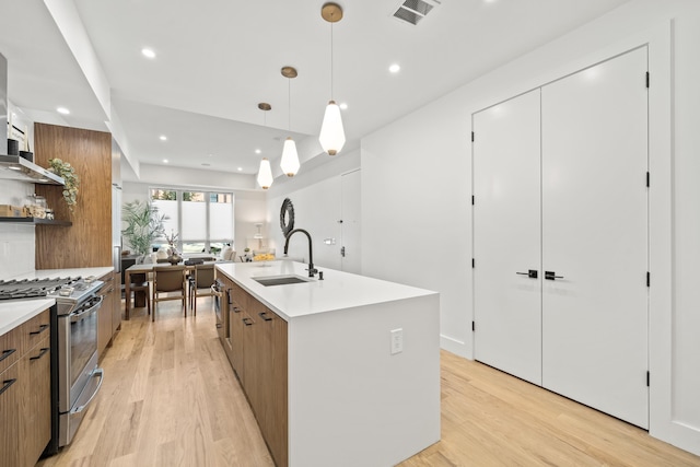 kitchen featuring a kitchen island with sink, sink, light wood-type flooring, decorative light fixtures, and gas stove