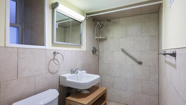 bathroom with tile walls, a tile shower, sink, and toilet