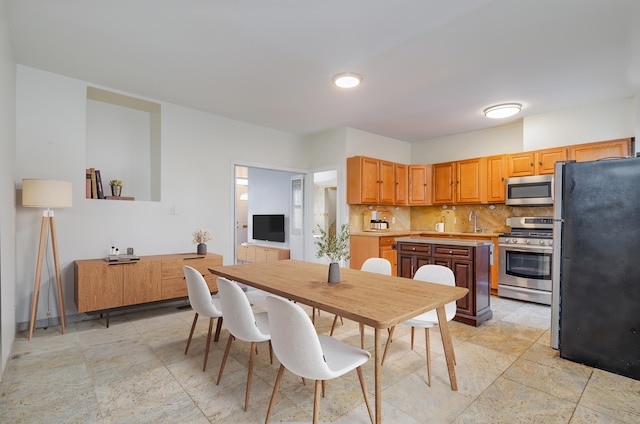 kitchen featuring a sink, light countertops, appliances with stainless steel finishes, tasteful backsplash, and stone finish floor