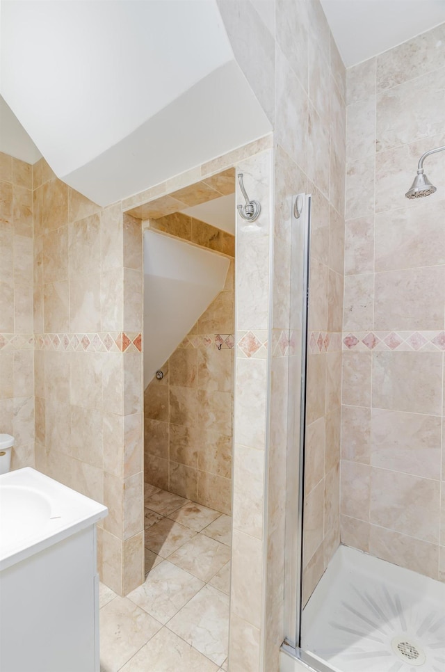 bathroom with a stall shower, vaulted ceiling, tile walls, and vanity