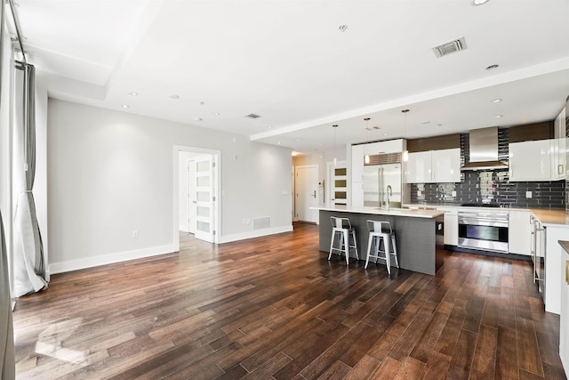 kitchen with a breakfast bar, stove, wall chimney range hood, white cabinets, and stainless steel built in refrigerator