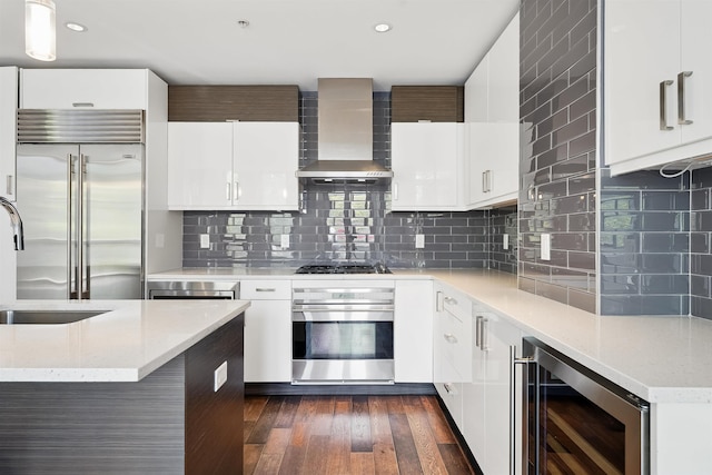 kitchen with decorative backsplash, dark wood-style flooring, wine cooler, wall chimney exhaust hood, and appliances with stainless steel finishes