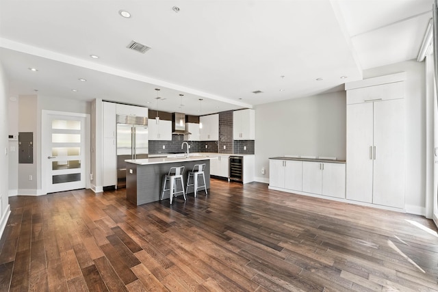 kitchen featuring decorative backsplash, a kitchen island with sink, a breakfast bar area, built in refrigerator, and beverage cooler