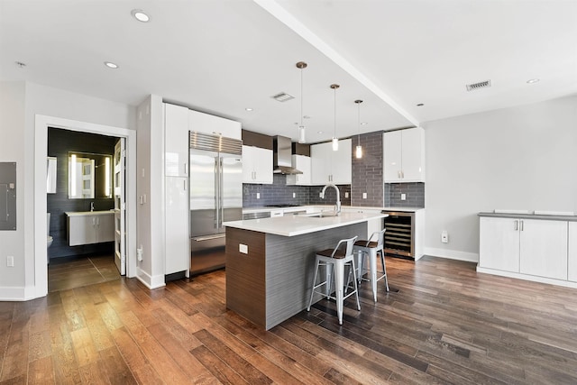 kitchen with visible vents, a sink, built in refrigerator, wine cooler, and wall chimney exhaust hood