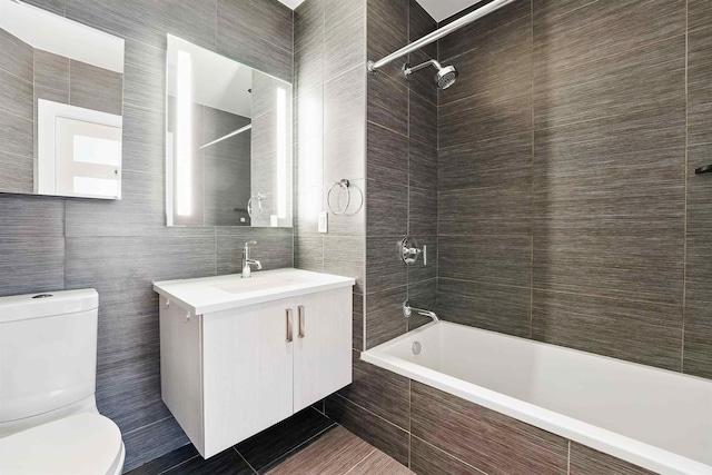full bath with vanity, tiled shower / bath combo, toilet, and tile walls