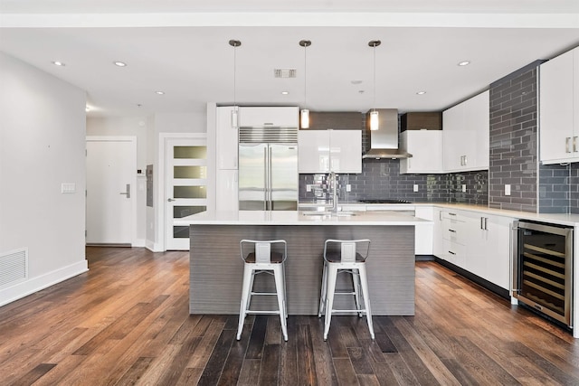 kitchen featuring a sink, beverage cooler, wall chimney exhaust hood, stainless steel built in fridge, and visible vents
