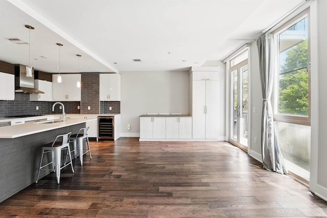 kitchen with decorative backsplash, wine cooler, light countertops, wall chimney exhaust hood, and a sink