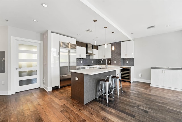 kitchen featuring wall chimney range hood, visible vents, a sink, built in refrigerator, and wine cooler