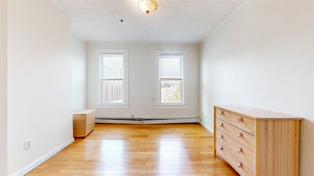 spare room with baseboard heating, light wood-type flooring, and ornamental molding