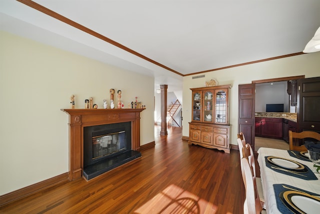 living area with visible vents, baseboards, dark wood finished floors, a glass covered fireplace, and crown molding