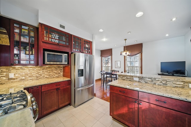 kitchen with stainless steel appliances, reddish brown cabinets, backsplash, and visible vents