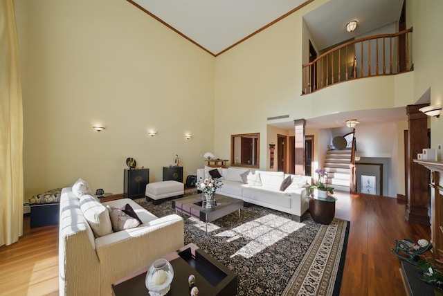 living room with wood finished floors, high vaulted ceiling, decorative columns, stairs, and crown molding