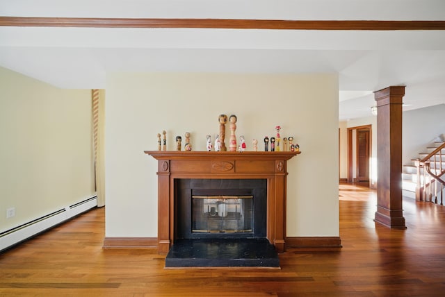 interior space with wood finished floors, baseboards, decorative columns, a glass covered fireplace, and baseboard heating