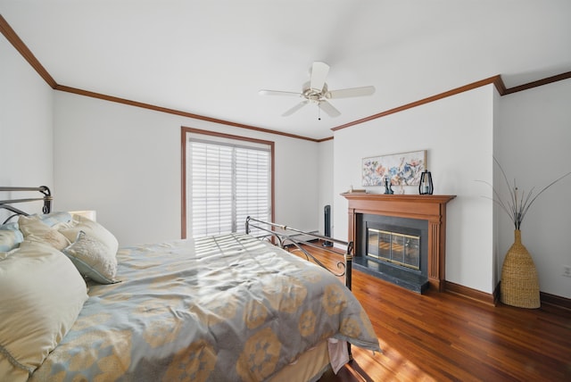 bedroom featuring ornamental molding, a ceiling fan, wood finished floors, a glass covered fireplace, and baseboards