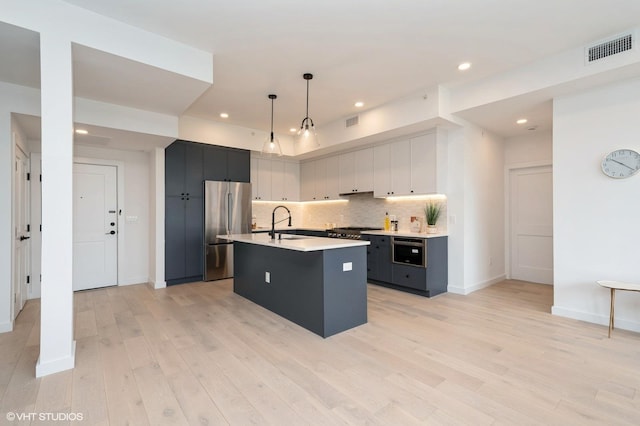 425 3rd St Unit 404, Jersey City, NJ 07302 - kitchen with stainless steel appliances, light countertops, backsplash, light wood-type flooring, and an island with sink