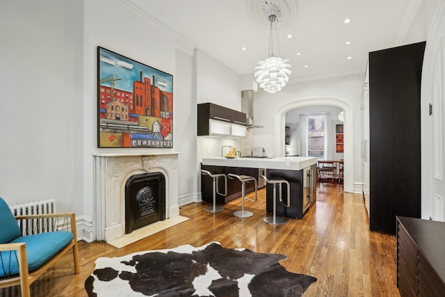 interior space with light hardwood / wood-style floors, a breakfast bar, radiator, crown molding, and wall chimney range hood