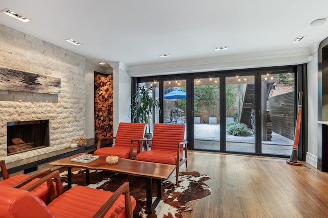 dining area featuring a stone fireplace, wood-type flooring, and ornamental molding