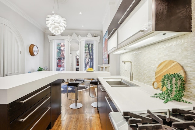 kitchen featuring ornamental molding, a notable chandelier, hanging light fixtures, sink, and light hardwood / wood-style floors