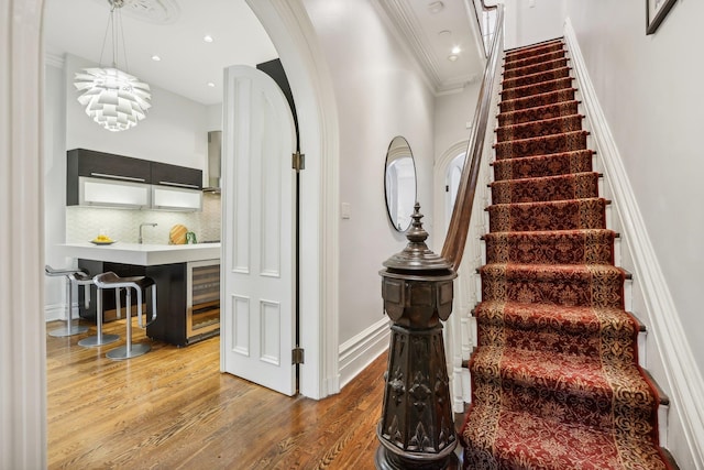 staircase featuring hardwood / wood-style flooring, wine cooler, an inviting chandelier, and crown molding